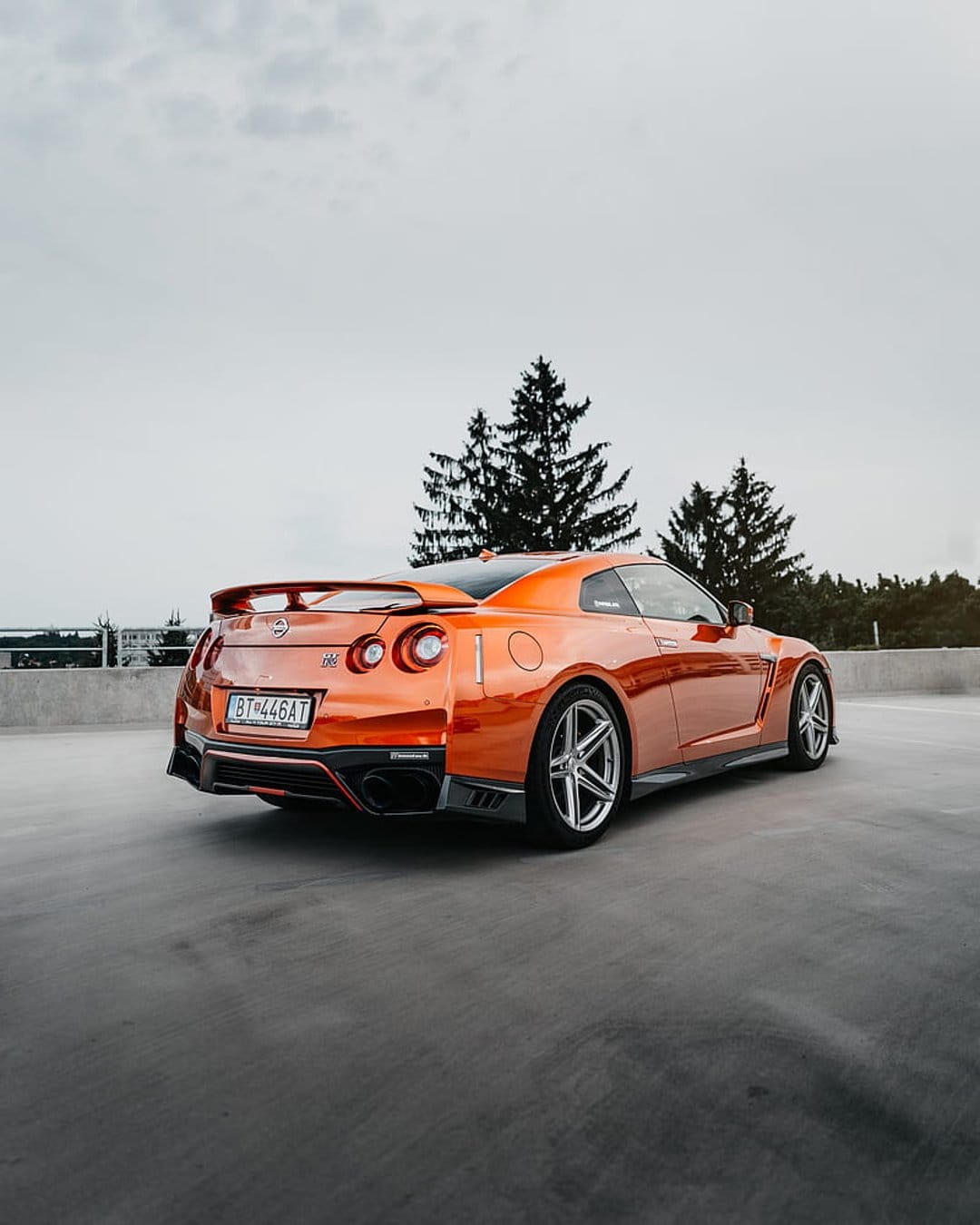 Orange Nissan GT-R rear view with round taillights and spoiler on a concrete rooftop under a grey sky.