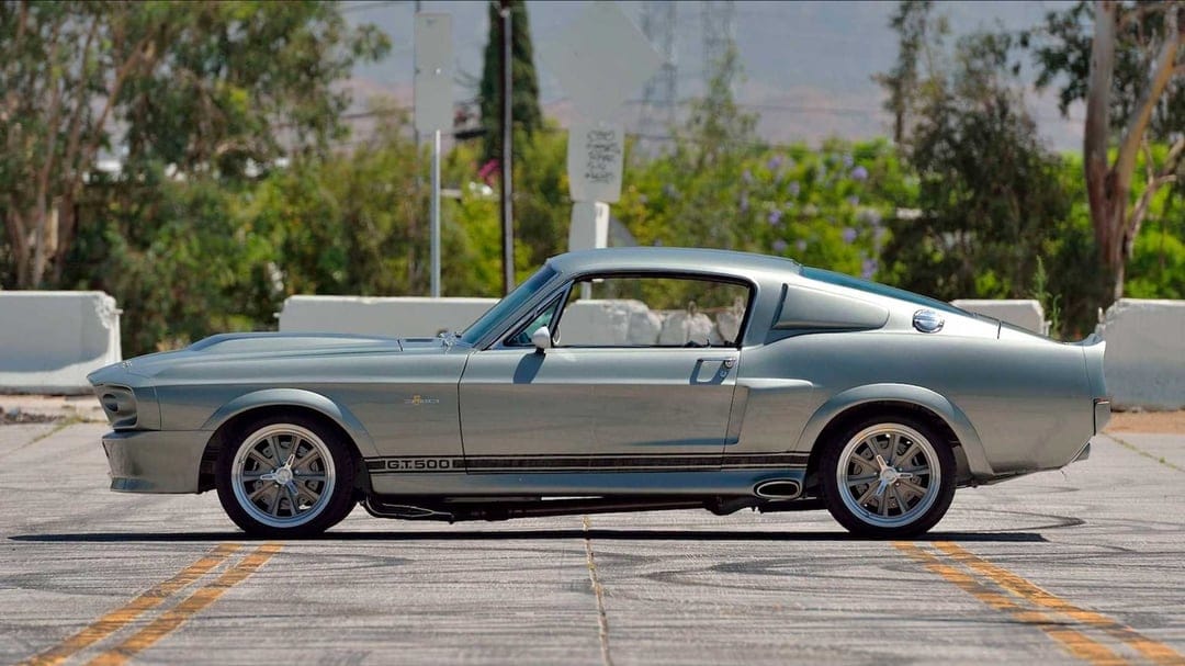 Metallic silver Shelby GT500 classic muscle car profile parked on asphalt with soft daylight reflections.