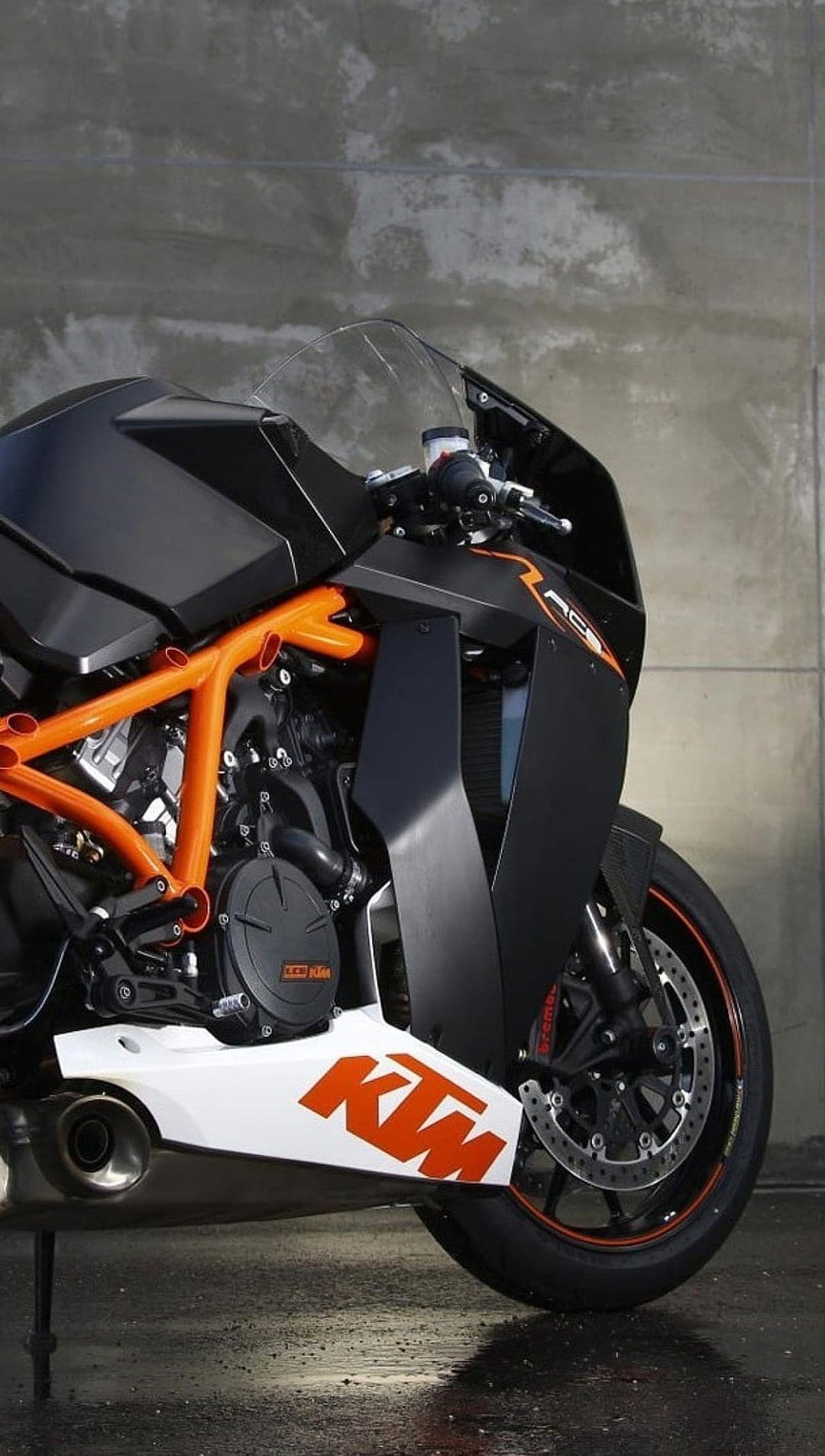 KTM superbike with an orange trellis frame and black fairings sits against a textured concrete wall backdrop.