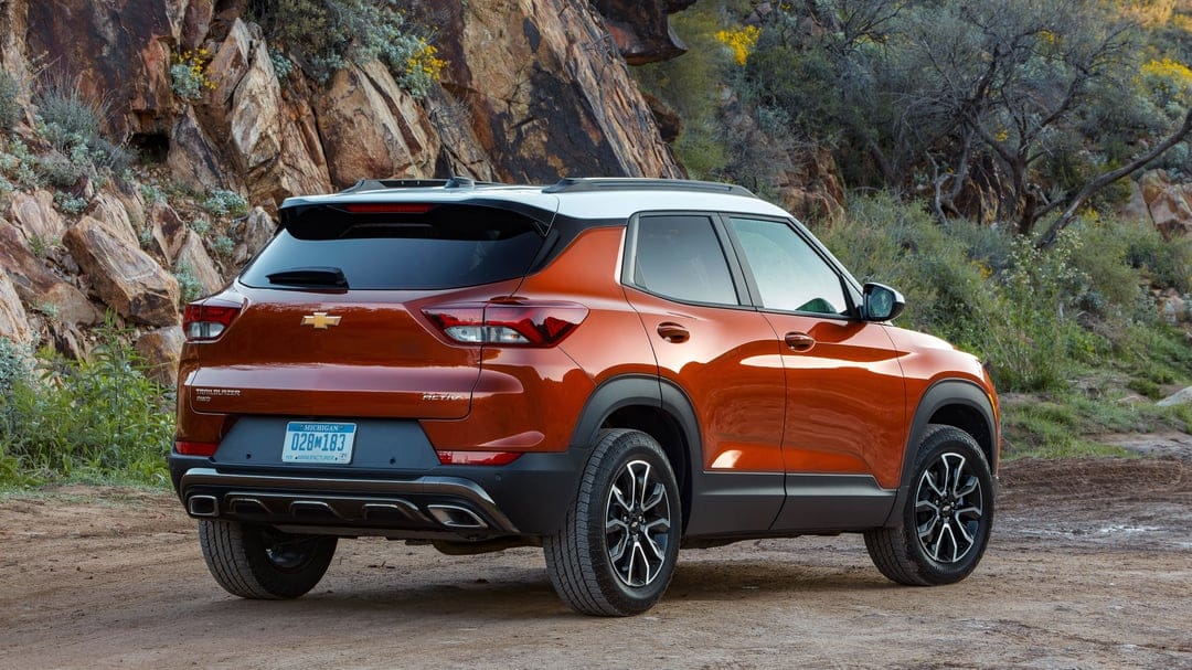 Burnt orange Chevrolet Trailblazer ACTIV with a white roof parked on a dirt path against rocky cliffs.