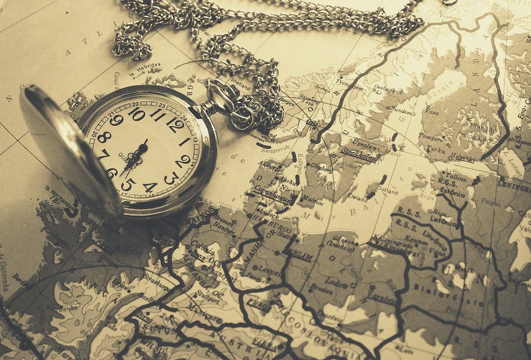 Brass pocket watch with a chain rests on a sepia-toned antique map of Europe showing old territorial borders.