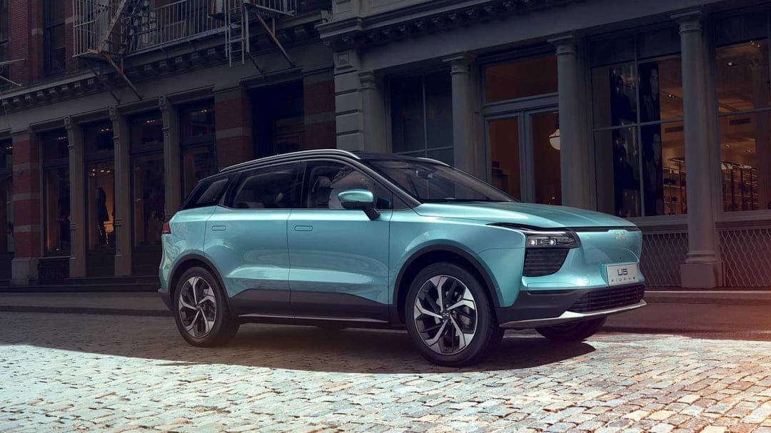 Teal AIWAYS U5 electric SUV parked on a cobblestone street in front of historic urban storefronts.