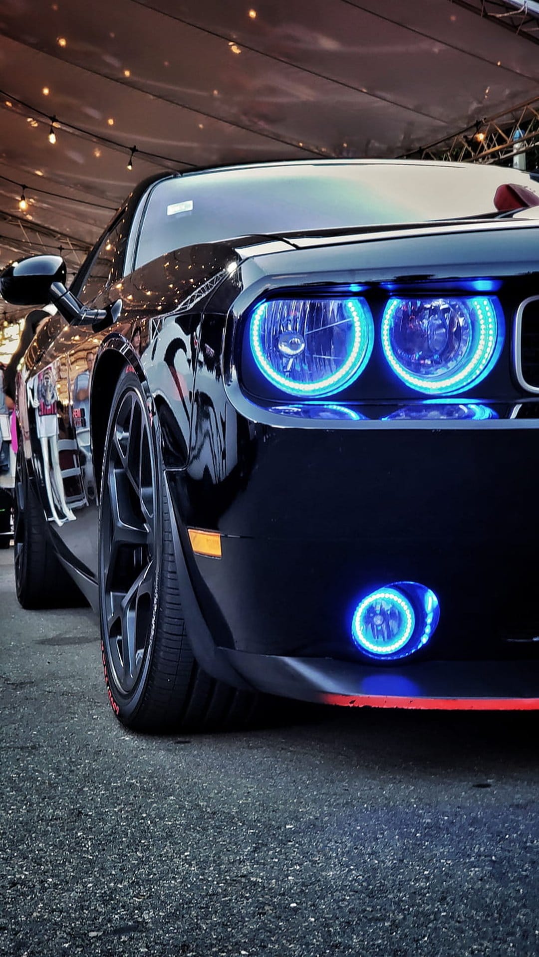 Black Dodge Challenger with glowing blue halo headlights, red bumper trim, and custom rims at night.