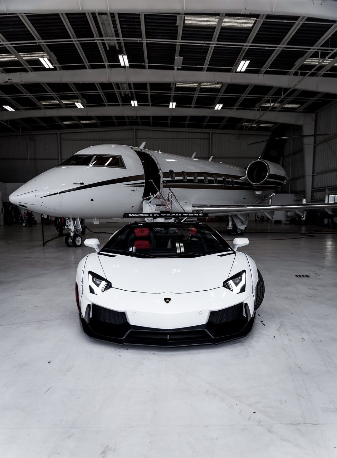 White supercar and private jet parked inside a modern hangar with polished floors and minimalist architecture.