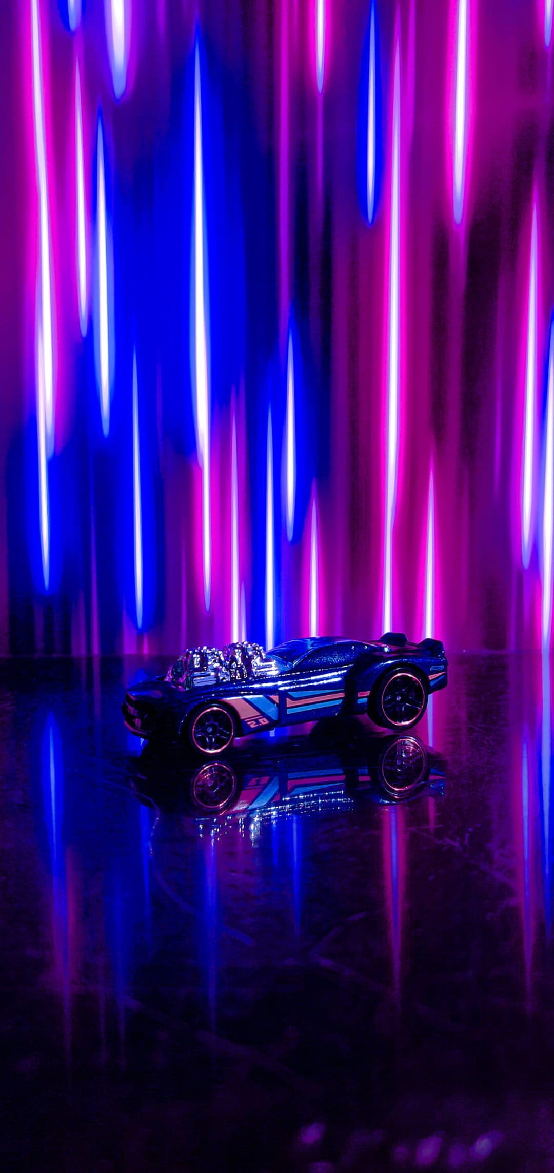 Blue miniature race car on a reflective surface with pink and blue neon light streaks in the dark background.