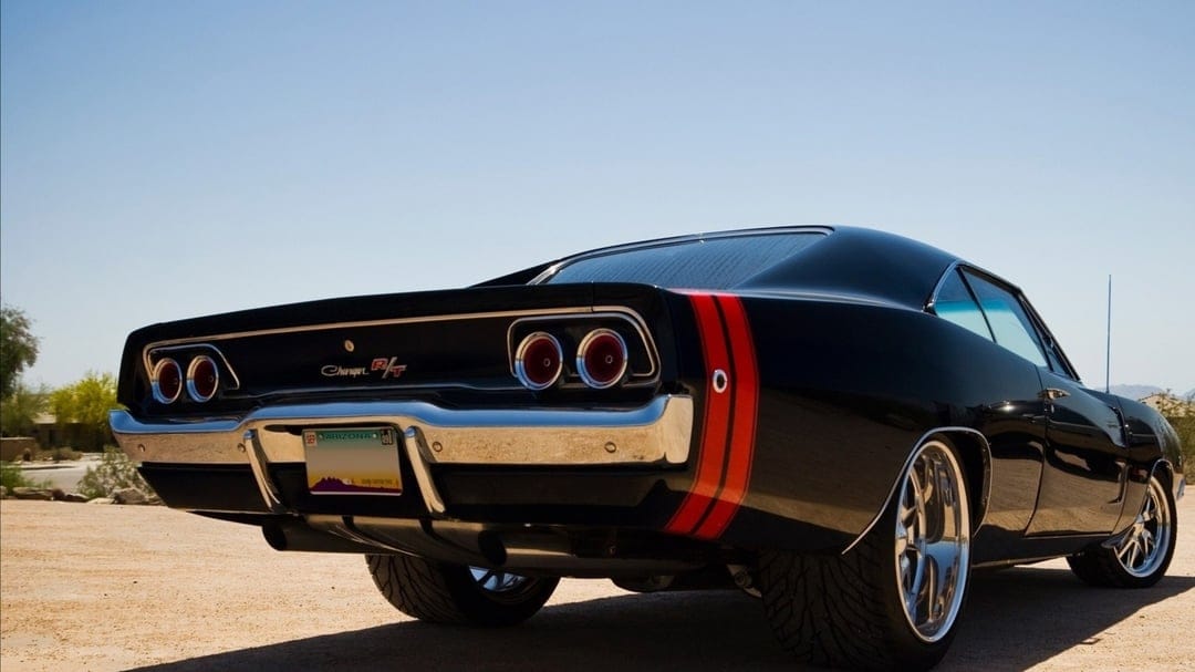 Black 1968 Dodge Charger R/T with red stripes on a desert path under a bright blue sky with chrome accents.