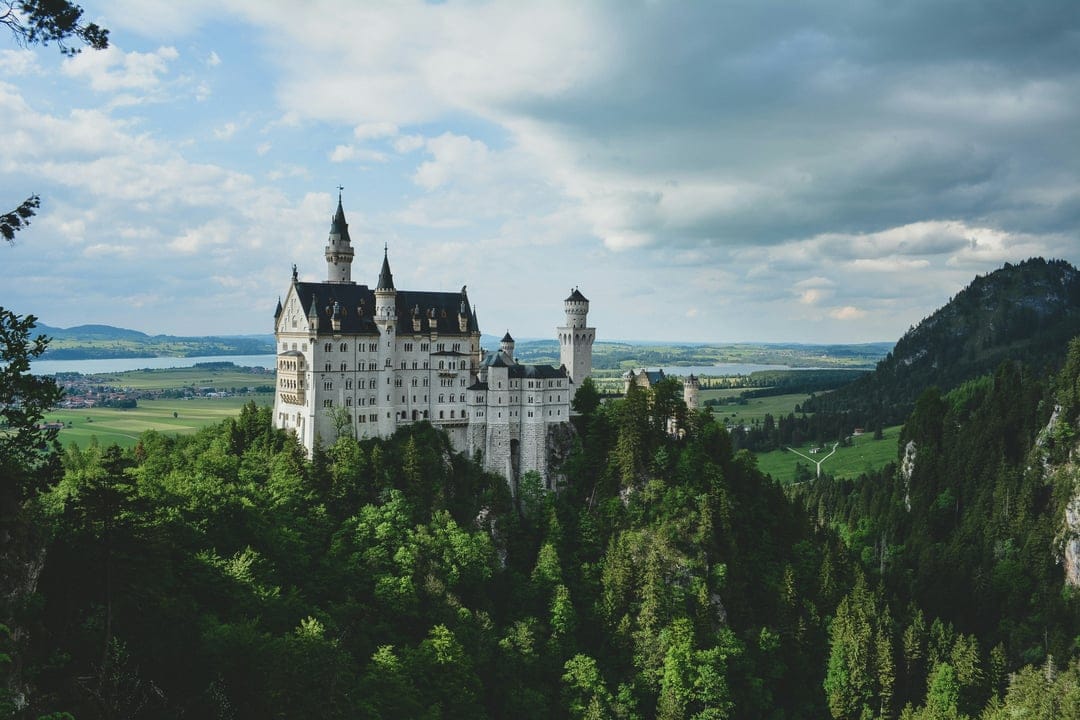 Neuschwanstein Castle with white stone towers surrounded by green pine trees and misty mountain peaks in Germany.