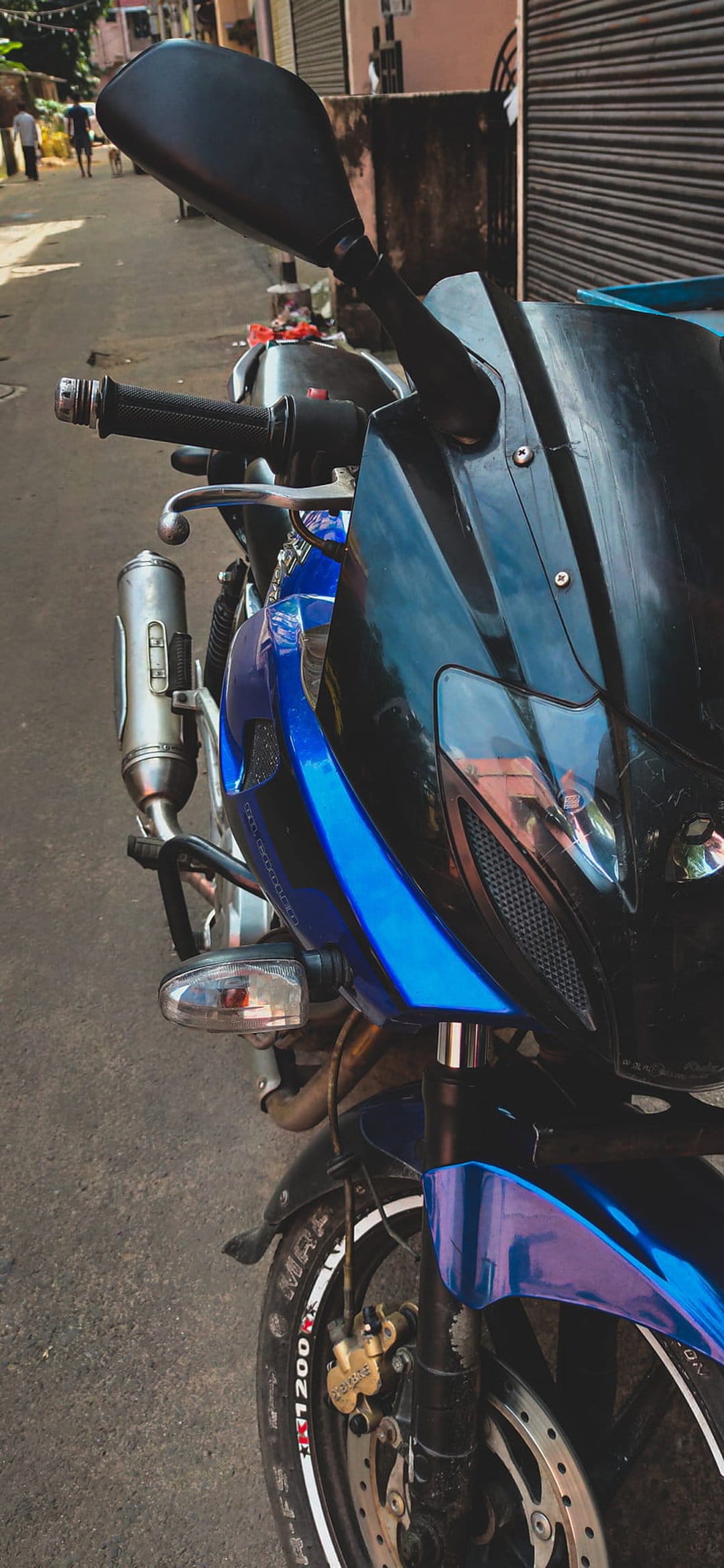 Blue and black motorcycle front fairing and handlebars on an asphalt road with a blurred urban city background.