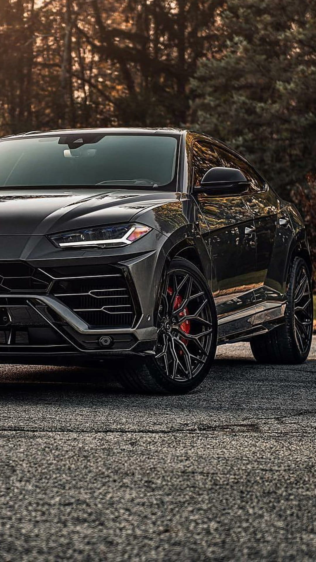 Black Lamborghini Urus SUV with sharp headlights and red brake calipers parked on a textured asphalt surface.