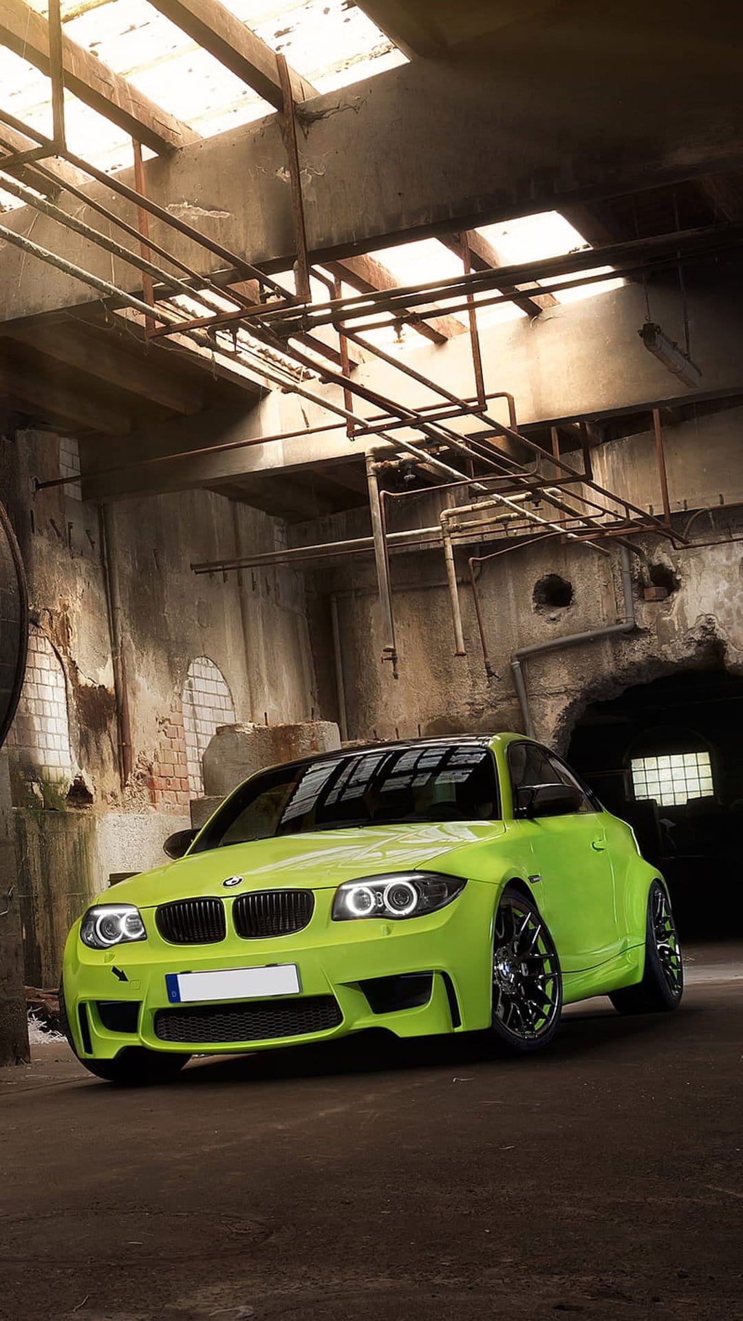 Lime green BMW coupe parked in a derelict industrial warehouse with concrete walls and overhead piping.