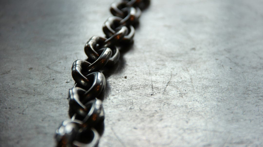 Interlocking polished steel chain links resting on a brushed gray metallic surface with soft background blur.