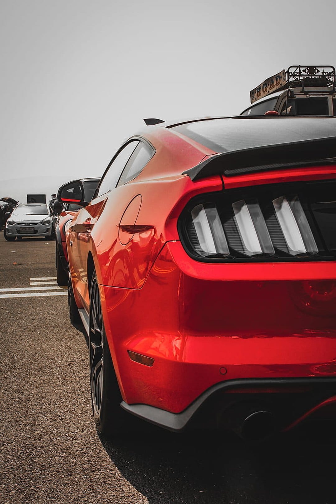 Red Ford Mustang rear showcasing triple LED taillights, black rear spoiler, and diffuser at an outdoor event.