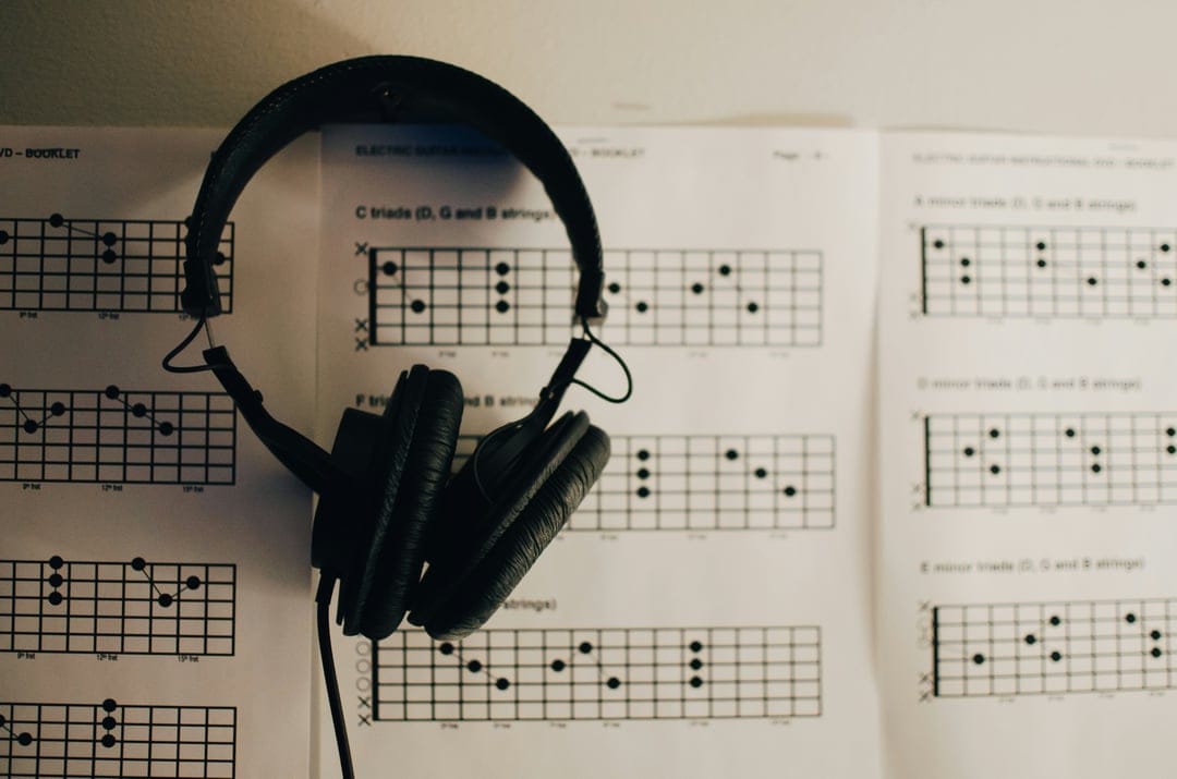 Black studio headphones resting on paper sheets displaying various guitar chord charts and musical notations.