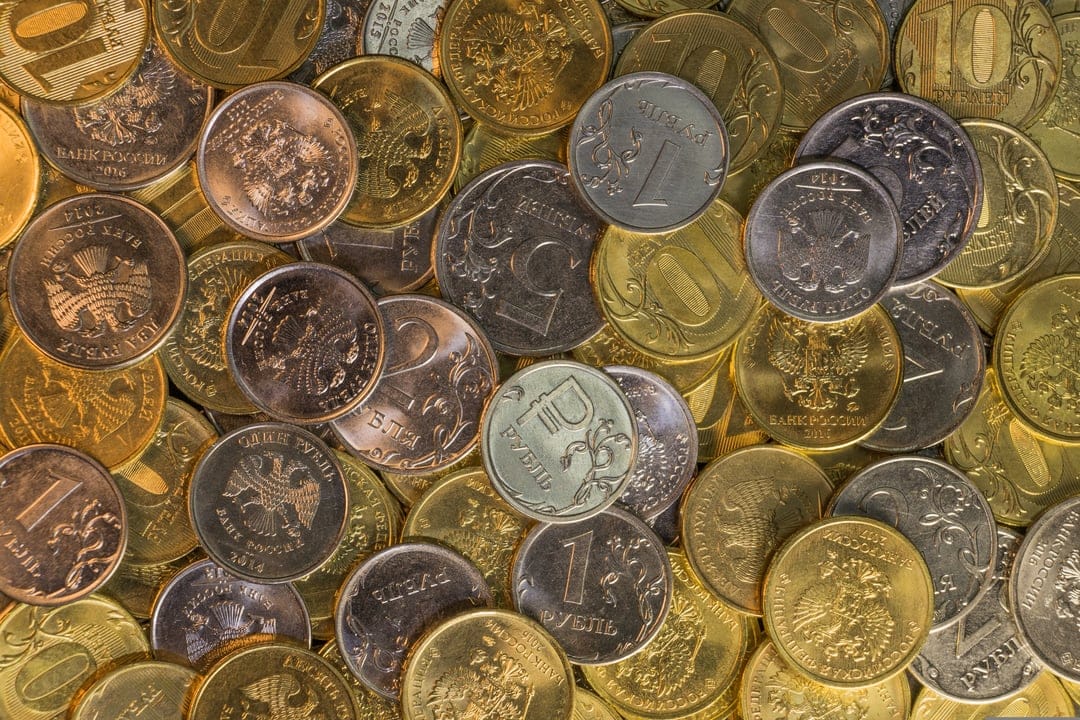 Russian ruble coins in a dense pile showing silver and gold metallic surfaces with engraved national emblems.