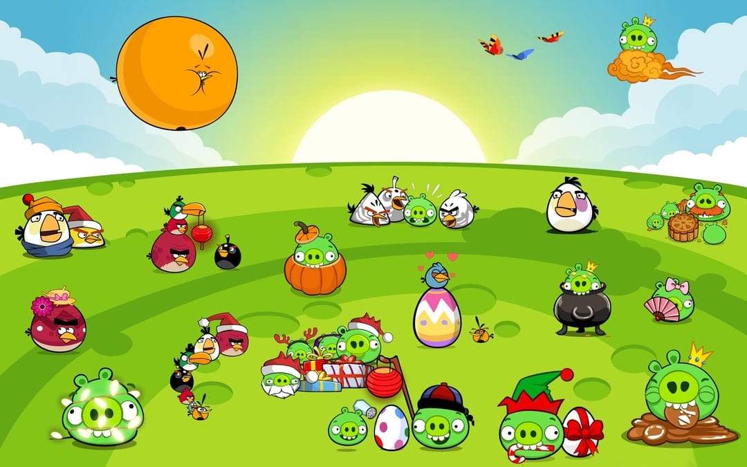 Angry Birds and Bad Piggies in festive costumes on a green hill under a bright yellow sun and blue sky.
