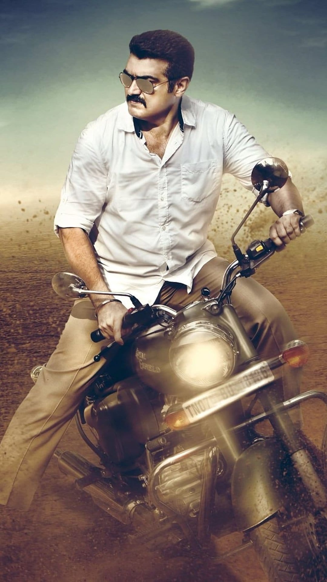 Man with a mustache and sunglasses rides a motorcycle through a dusty desert landscape with a blurred background.