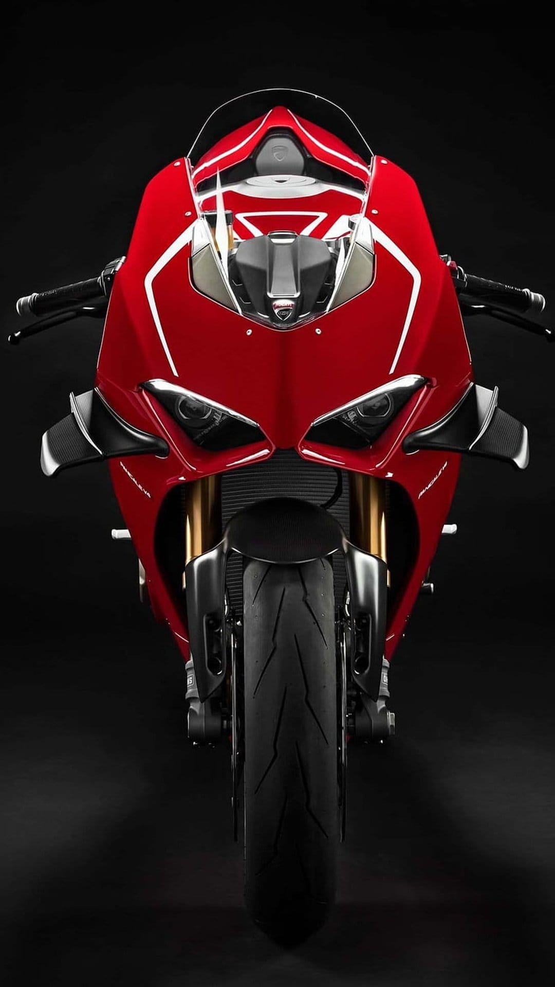 Red Ducati motorcycle facing forward with lit headlights and sleek fairings against a pitch black backdrop.