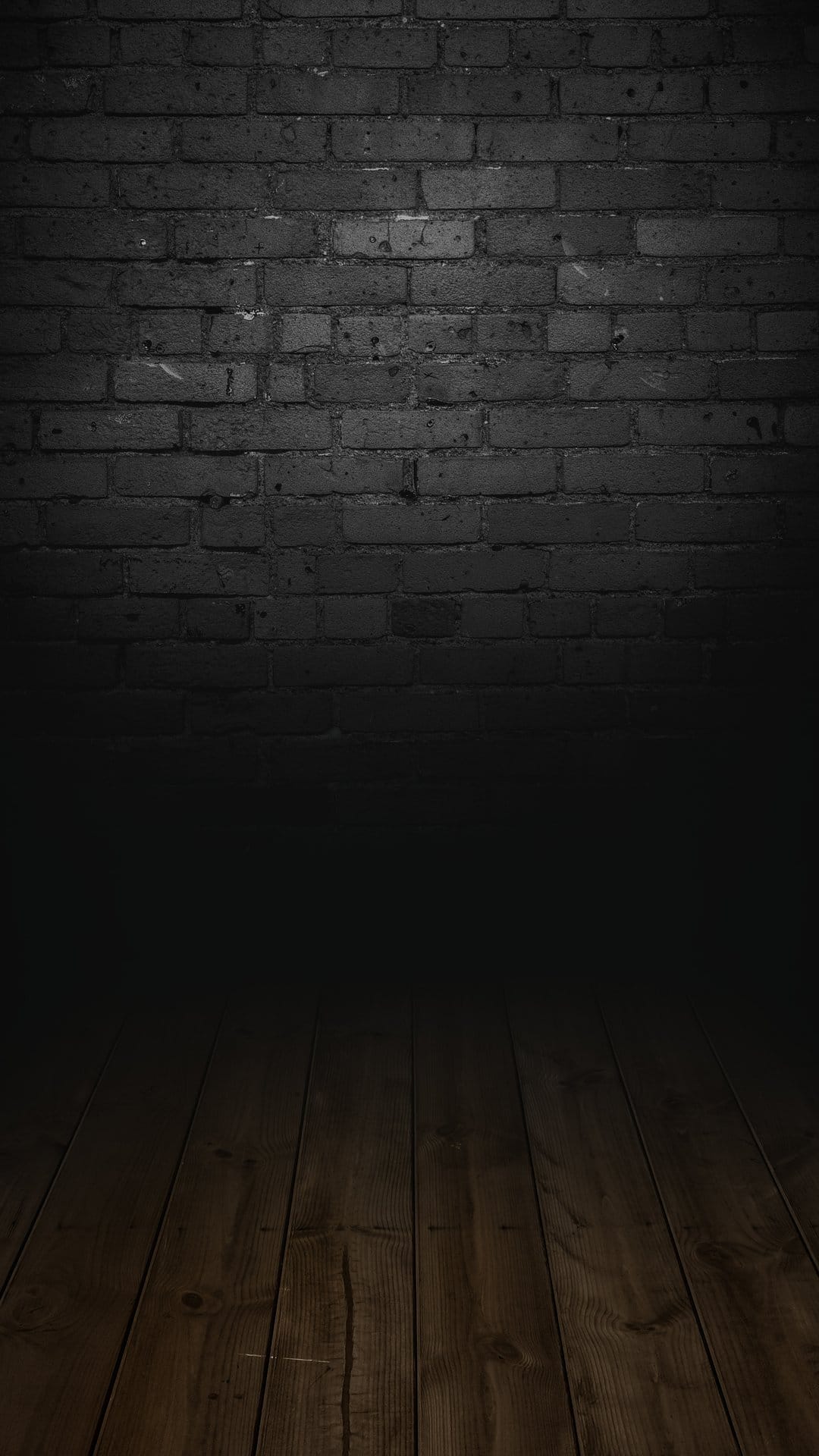 Dark brick wall fading into heavy shadows above a textured wooden floor with visible grain in a vertical frame.