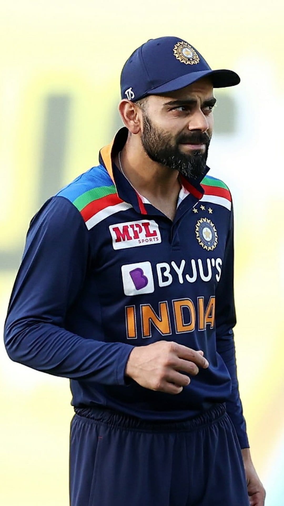 Virat Kohli wearing a blue Indian cricket cap and national team jersey with an intense facial expression.