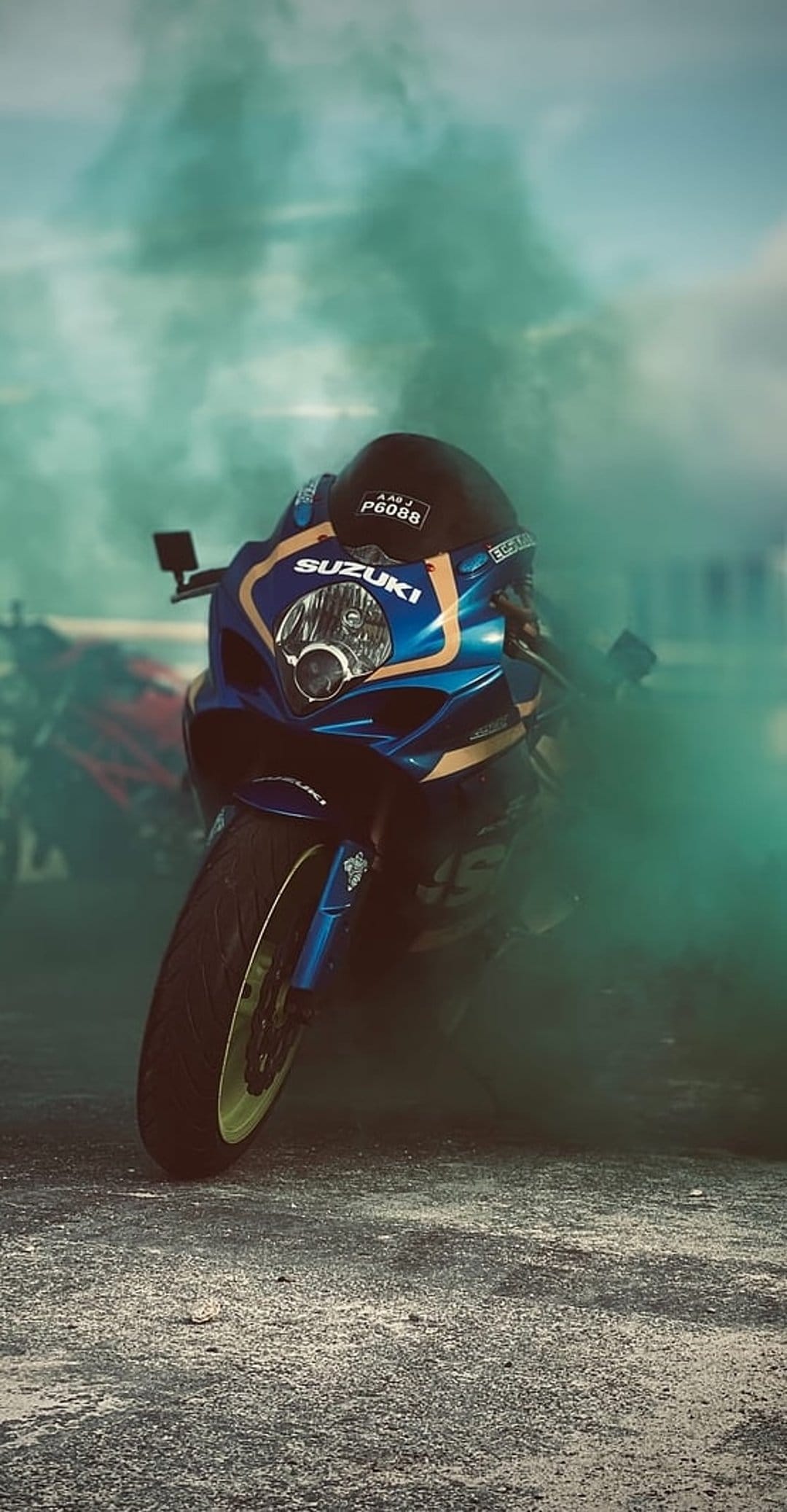 Blue Suzuki motorcycle with visible logo emerges from thick swirling green smoke against a blurred background.