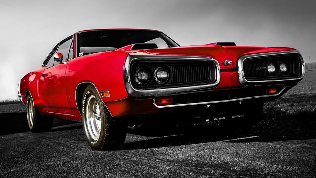 Red 1970 Dodge Coronet Super Bee muscle car with chrome grille and dual hood scoops on a dark asphalt road.