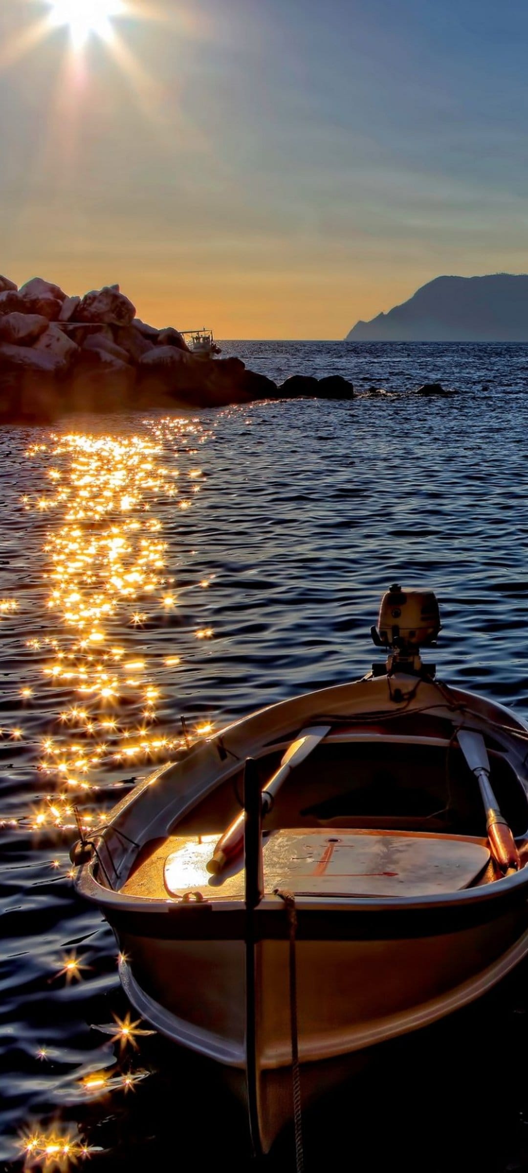 Small motorboat on rippling water during a golden sunset with distant mountains along the jagged shoreline.