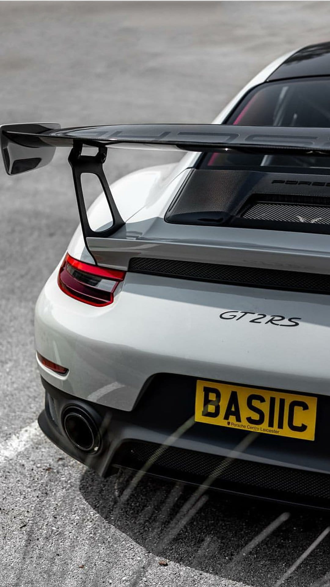 Porsche 911 GT2 RS rear view featuring a large carbon spoiler, white bodywork, and a yellow BASIIC license plate.