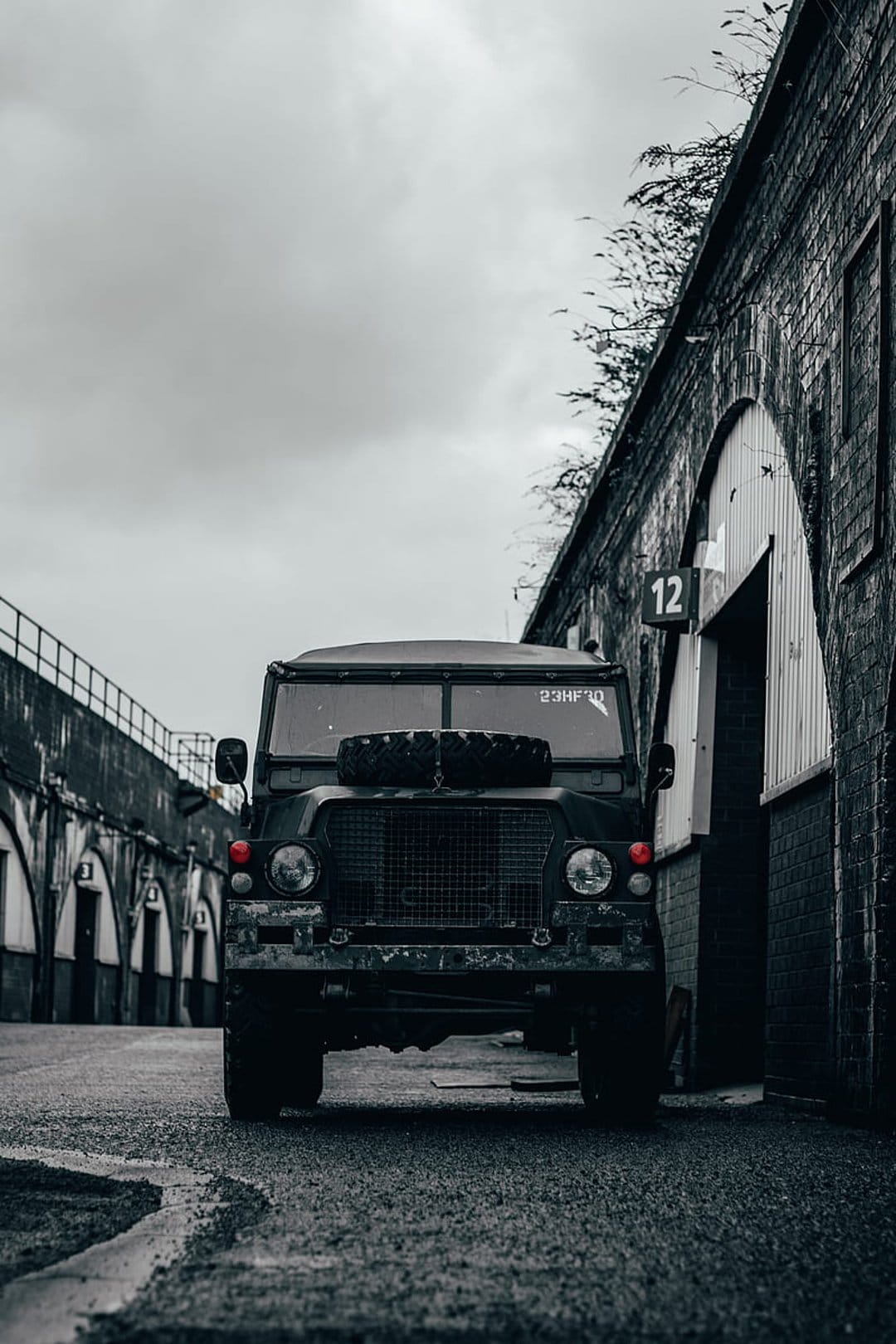Land Rover Defender with a hood spare tire parked in a dark brick tunnel with arched doorways in monochrome.