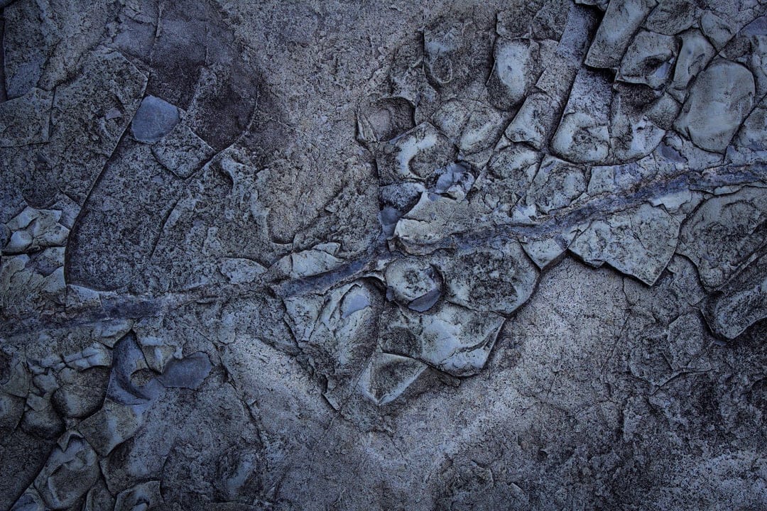 Deep blue and gray rock fissures show jagged cracks and weathered mineral textures in a vertical close-up shot.