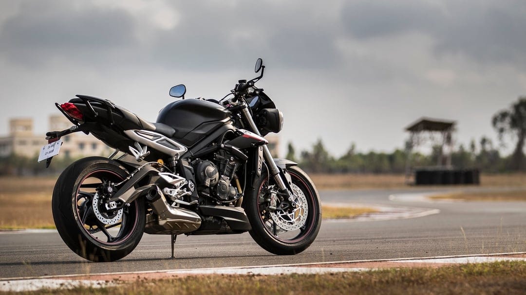 Black sport motorcycle parked on a racetrack curve under a cloudy sky with red tail light and silver exhaust.