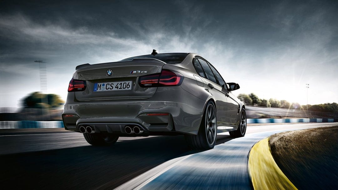Grey BMW M3 CS sports sedan speeding around a race track curve with motion blur and cinematic lighting.