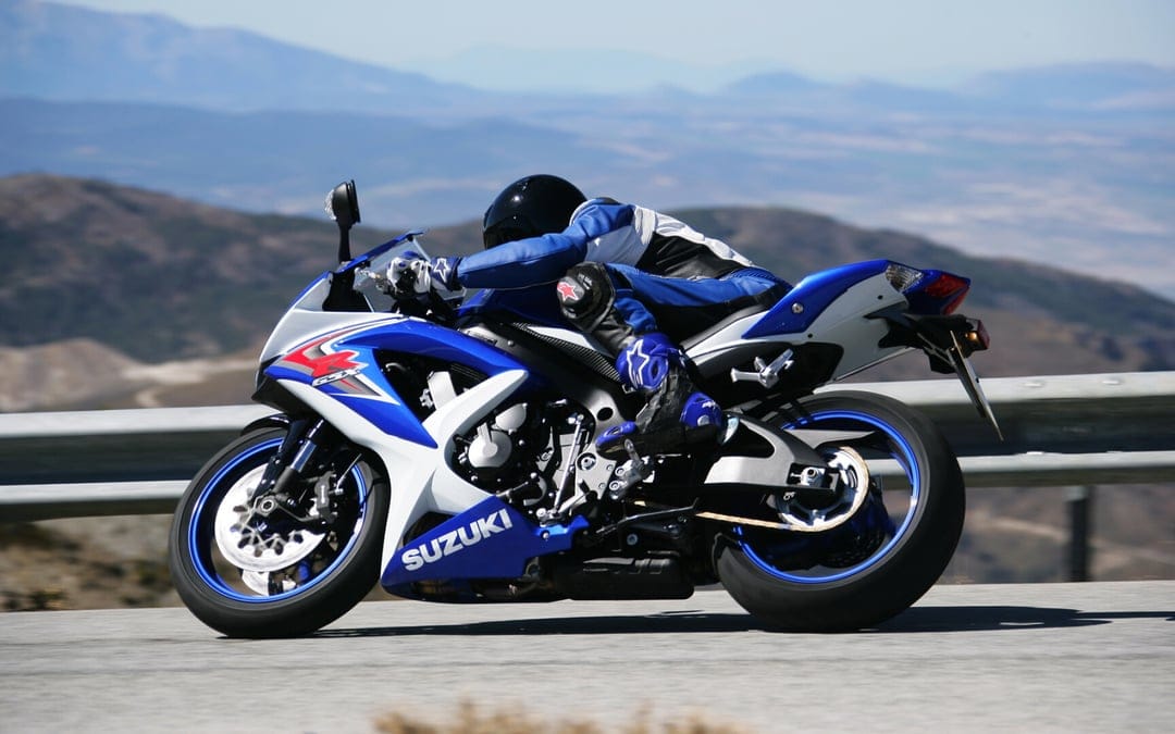 Blue Suzuki sportbike leaning into a mountain curve with a rider in a matching blue and black racing suit.