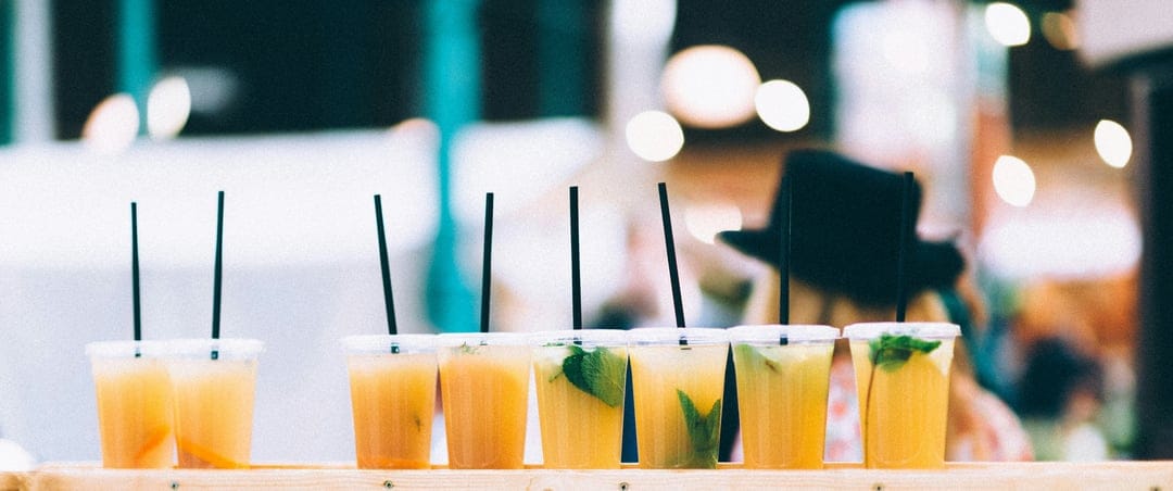 Yellow and orange citrus drinks in clear cups with black straws and mint leaves arranged on a wooden surface.