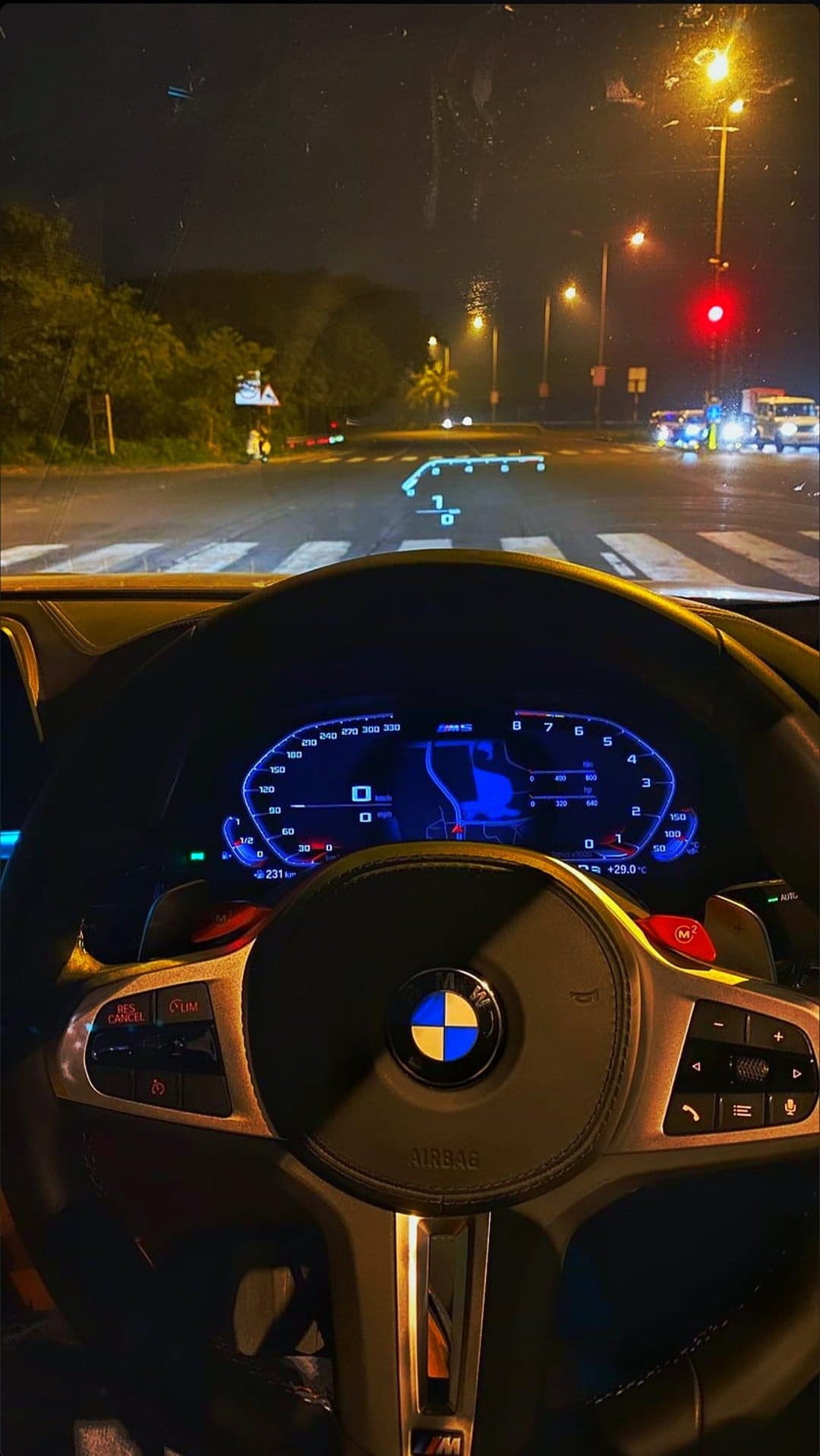 BMW steering wheel and digital dashboard glow in a dark car interior with a head-up display on the glass.