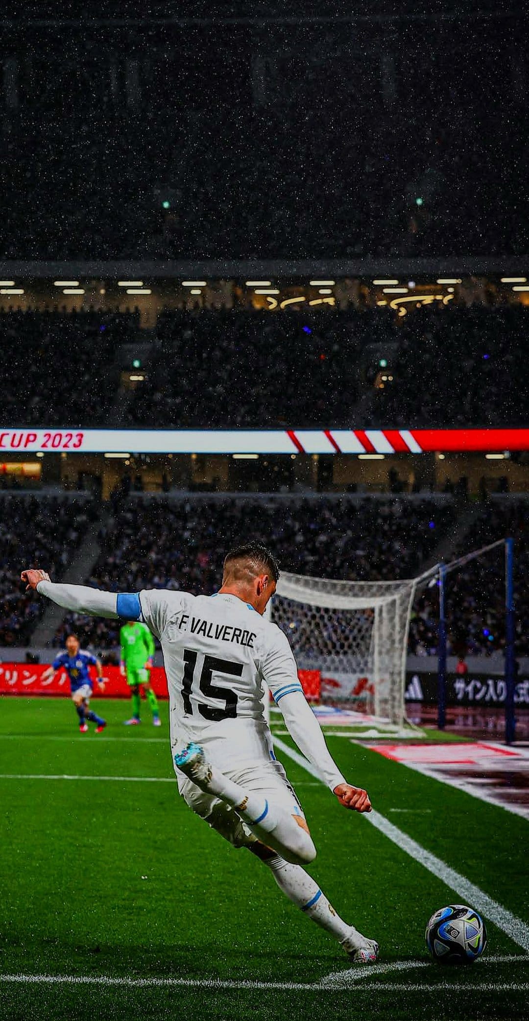 Federico Valverde kicks a soccer ball on a wet grass field during a rainy match in a lit stadium at night.
