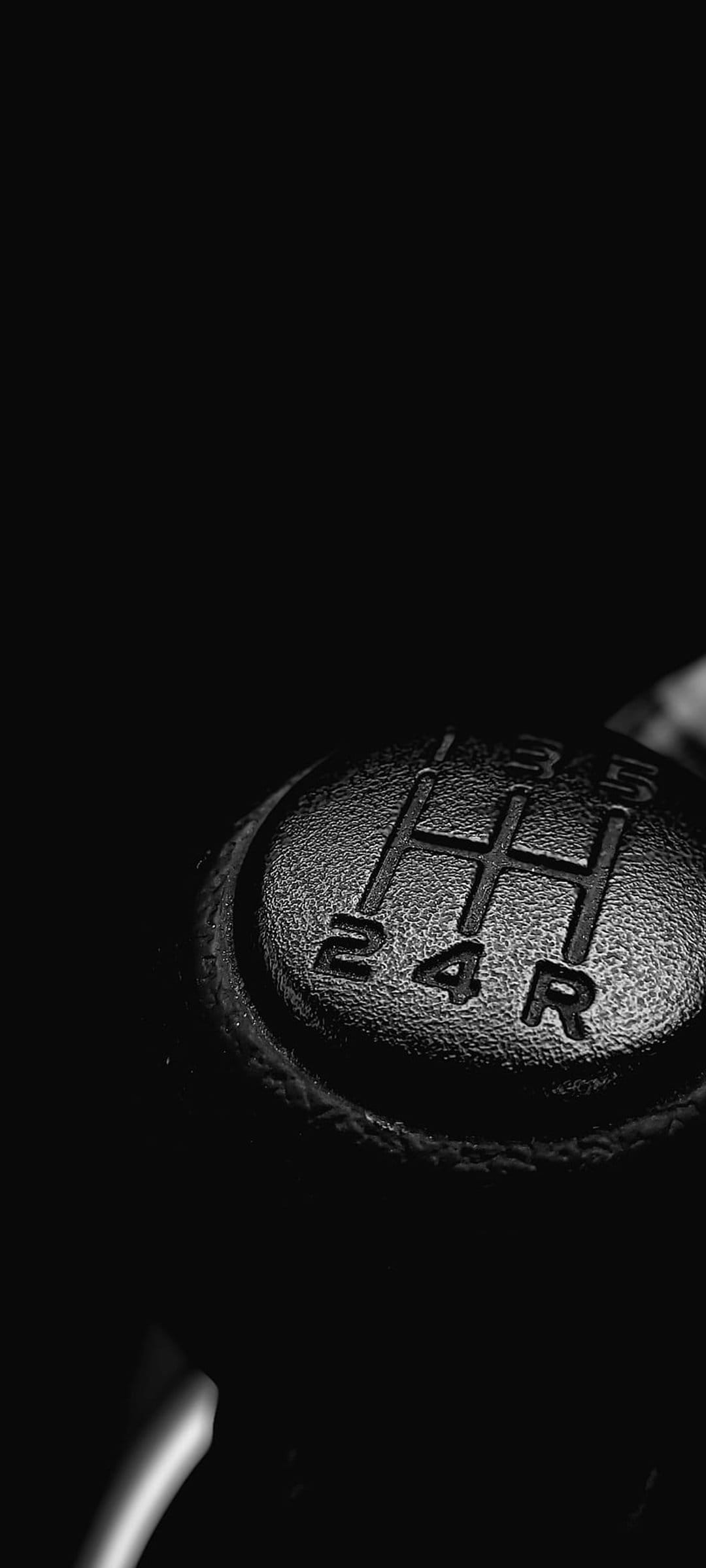 Black gear shift knob with white engraved shift patterns sits against a dark, out-of-focus car interior background.
