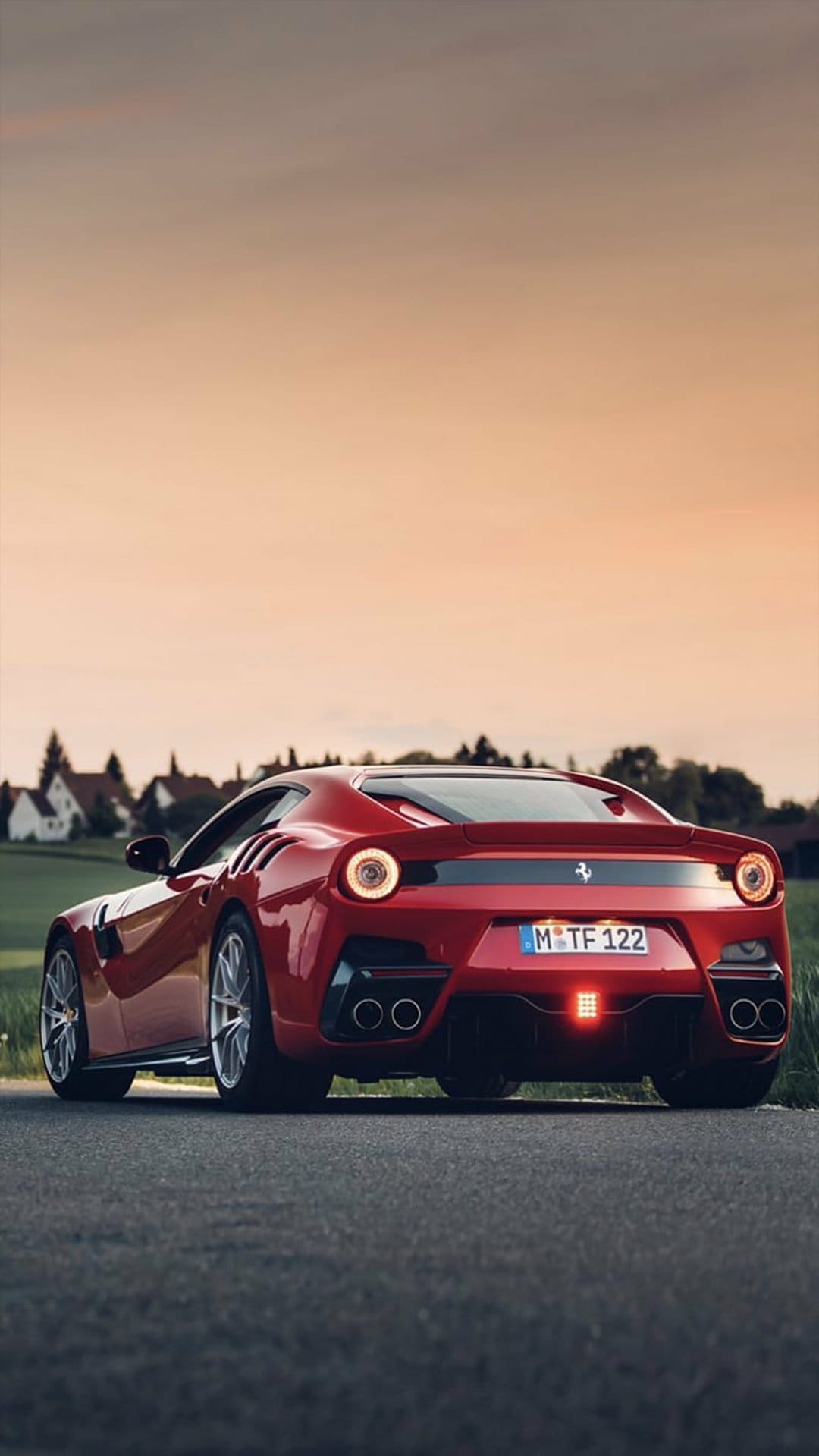 Ferrari F12 Berlinetta in red parked on a country road at sunset with visible quad exhausts and round taillights.