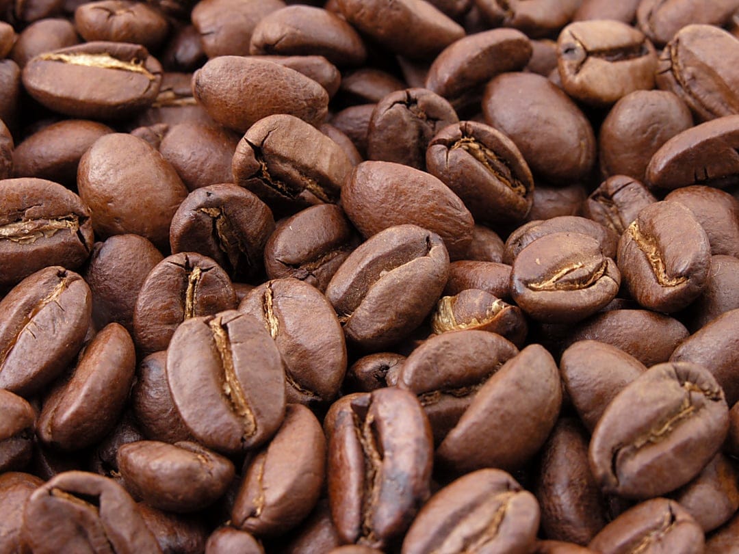 Roasted coffee beans show intricate grooves and glossy textures in a tight macro shot with deep brown tones.