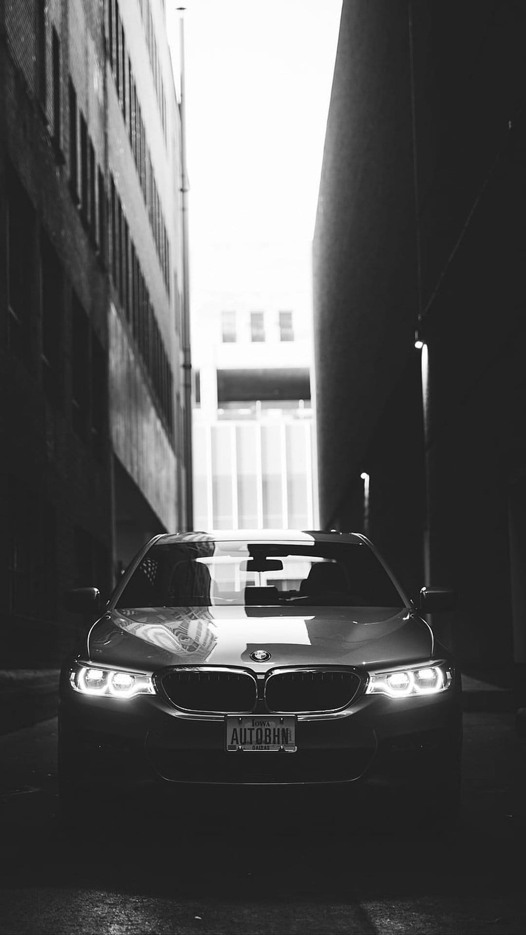 Modern BMW parked in a dark urban alley with glowing headlights, high contrast shadows, and tall buildings.