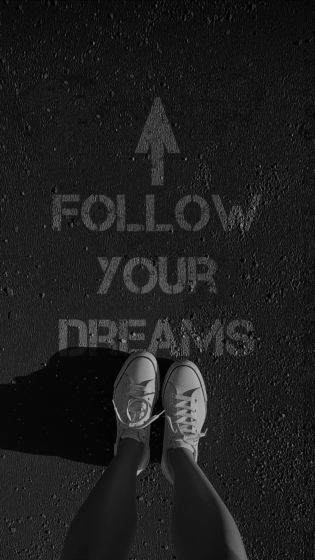 White canvas sneakers stand on dark pavement next to stenciled text saying Follow Your Dreams with an arrow.