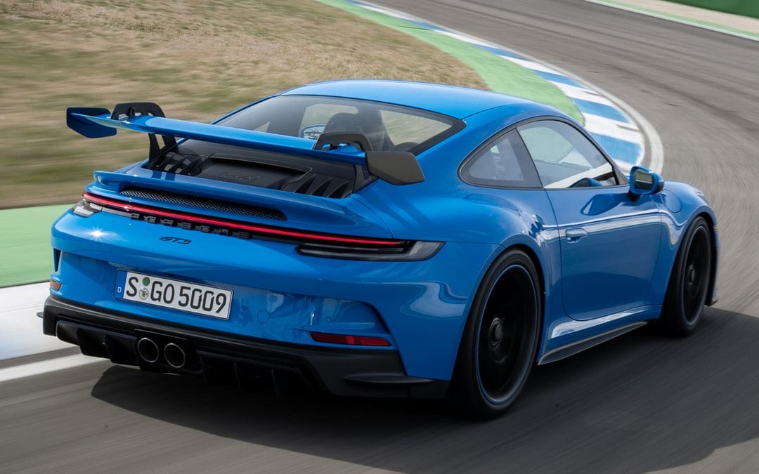 Blue Porsche 911 GT3 with a swan-neck wing driving through a curved racetrack corner with motion blur.