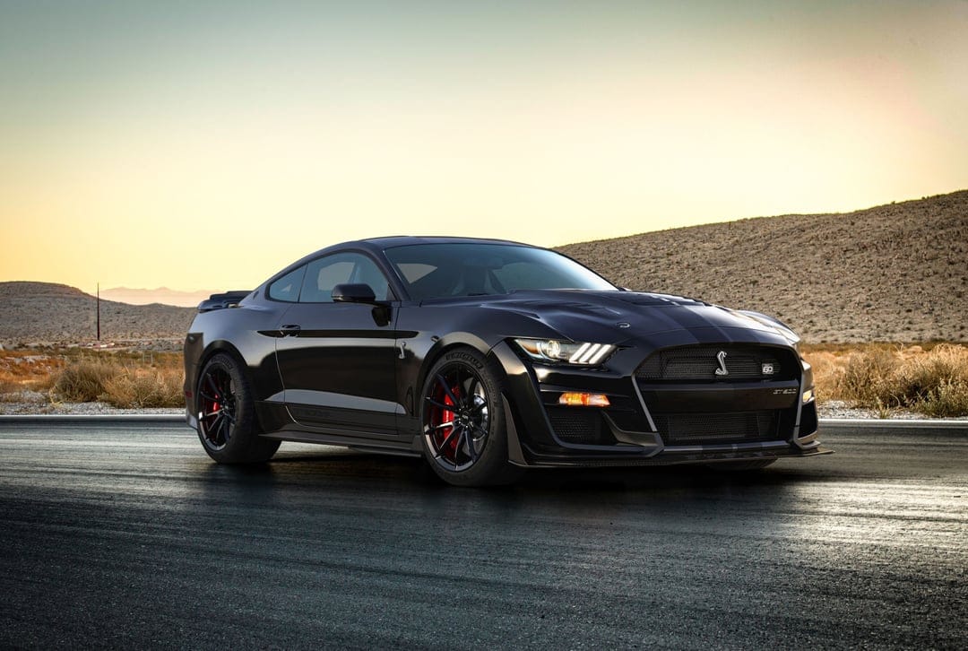 Black Shelby GT500KR sports car on an asphalt road with desert hills and golden sunset light in the background.