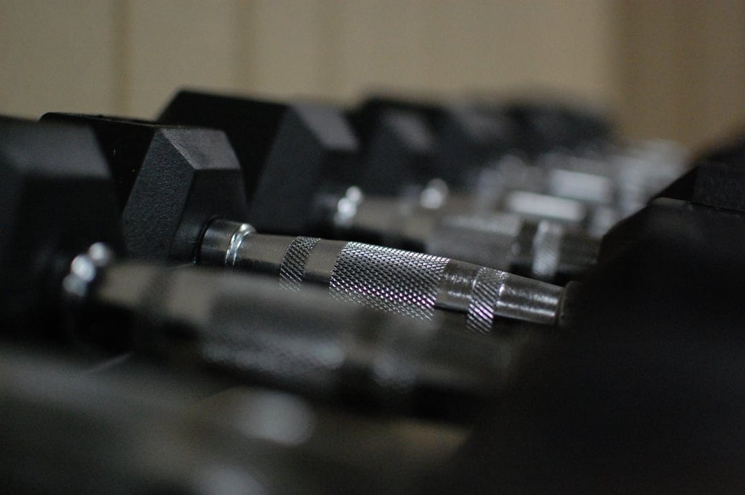 Chrome knurled dumbbell handles on a metal rack with a blurry gym background in a vertical close-up shot.