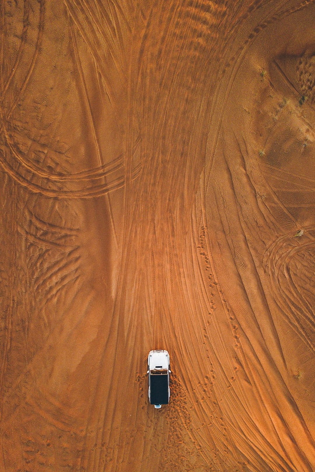 Monochrome vehicle driving through vast sand dunes leaving tire tracks across the golden desert surface.