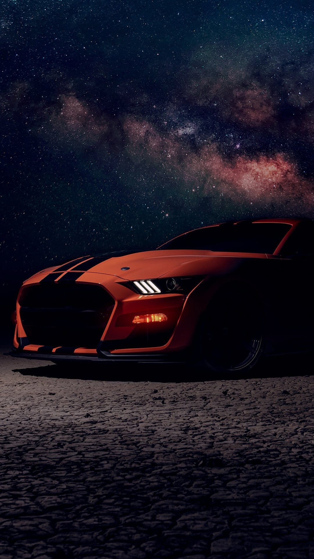 Orange muscle car with black stripes parked under a purple Milky Way galaxy filled with glowing stars.