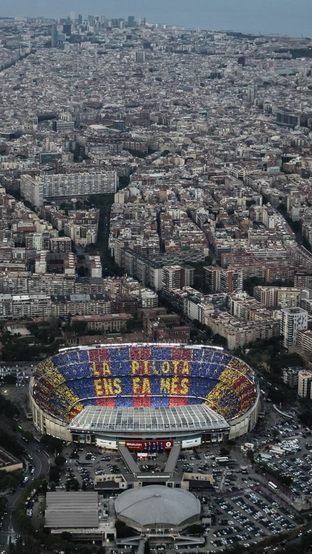 Camp Nou stadium showing blue and red seating patterns surrounded by the geometric urban grid of Barcelona city.