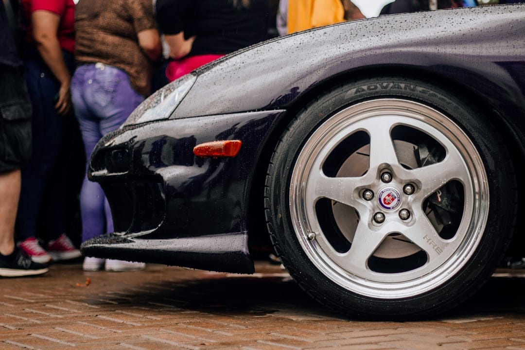 Silver five-spoke wheel on a dark purple sports car with Advan tires at an outdoor automotive event.