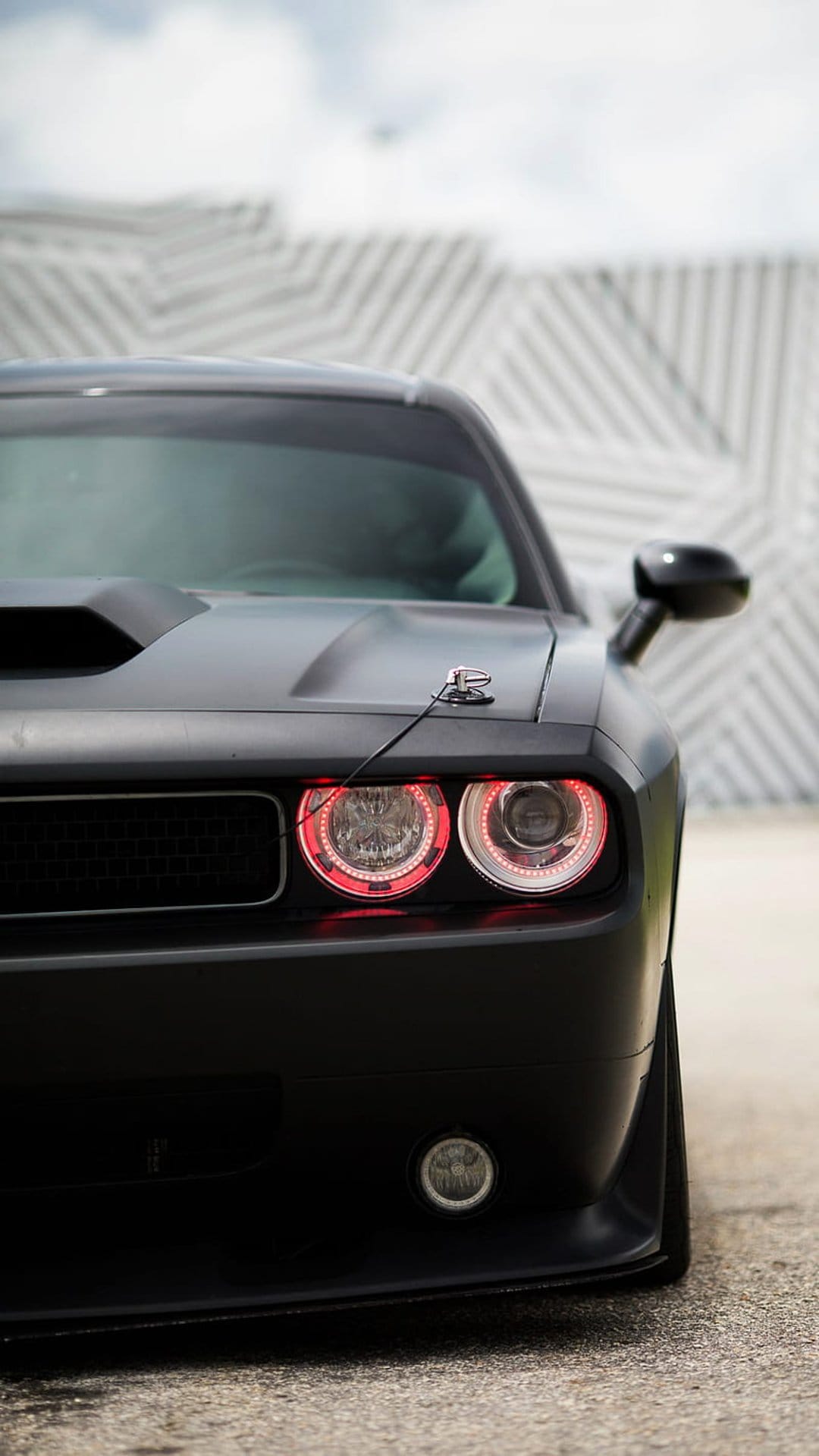 Dodge Challenger front end with red halo headlights and matte black paint against a geometric wall background.