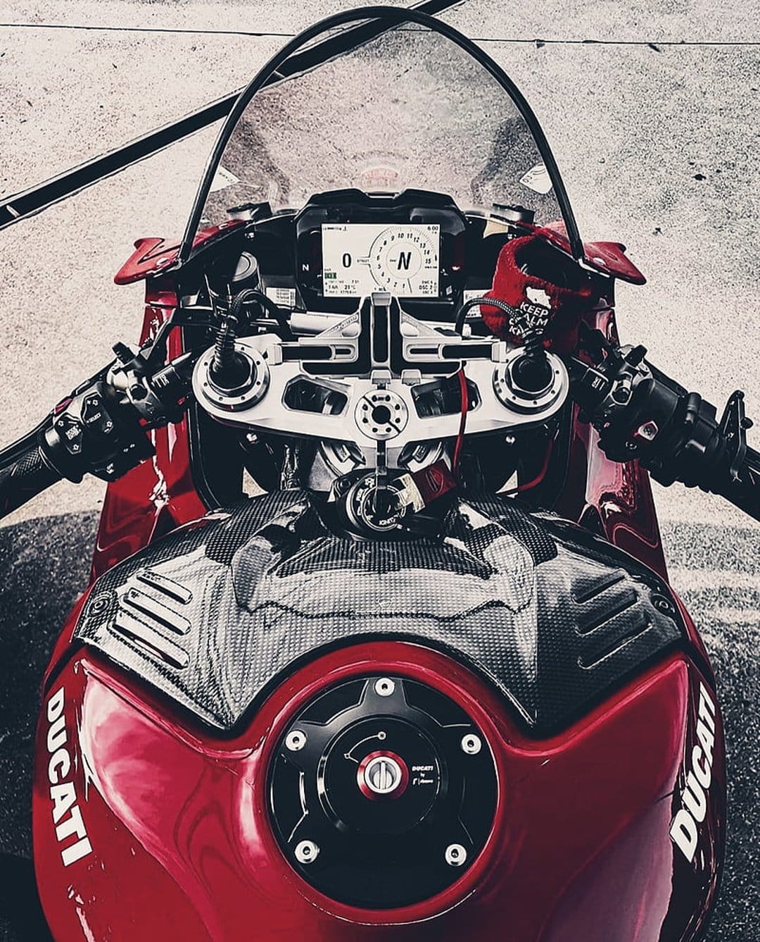 Red Ducati fuel tank and digital dashboard with carbon fiber details and clip-on handlebars in a close-up shot.