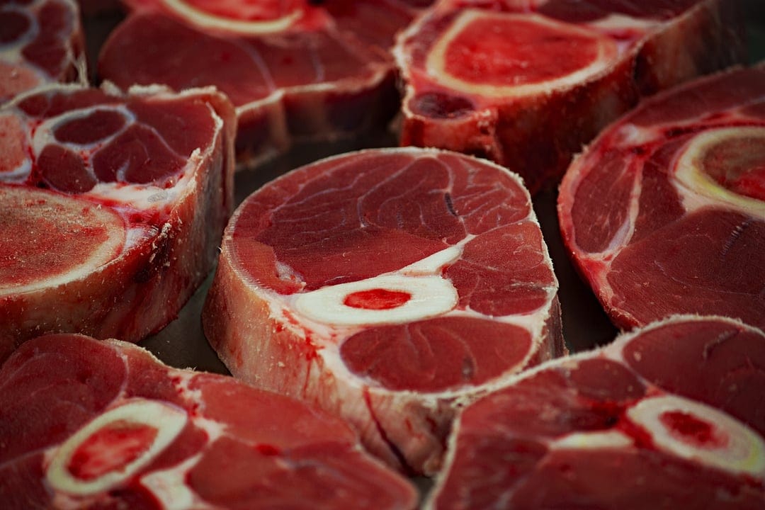 Raw beef shank cross-sections with white marrow bones show deep red muscle texture and ivory fat marbling.